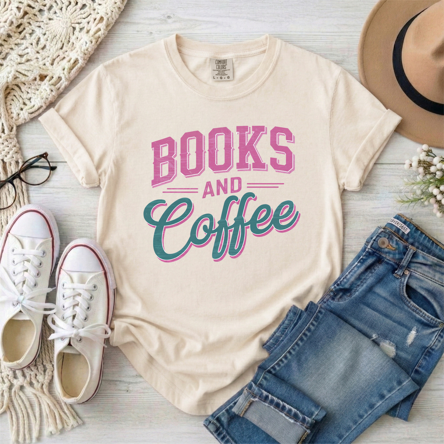 Beige t-shirt with 'Books and Coffee' text, paired with jeans, sneakers, and a hat on a light wooden surface.